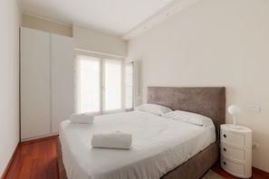 A bedroom with a bed, a wardrobe, a bedside table, and a window.