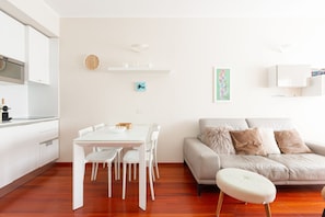 A modern kitchen with white cabinets, a dining table with chairs, a sofa, and a small ottoman.