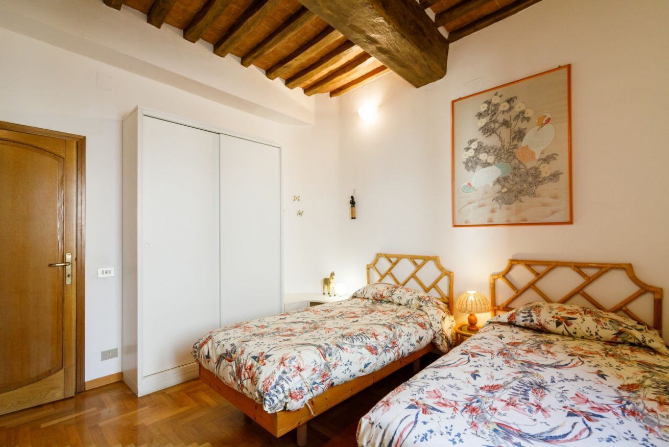 Une chambre avec deux lits en bois, un plafond en bois, une armoire blanche et un tableau accroché au mur.