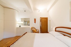 Une chambre à coucher avec un lit, une tête de lit en bois, une porte en bois, une armoire blanche, une commode, une chaise et un miroir.