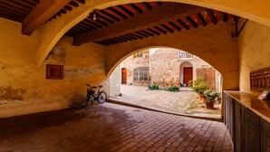Un corredor arqueado con una bicicleta, un banco de madera y vista a un patio con un edificio al fondo.