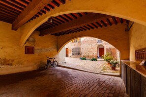 Un couloir en arc de cercle où l’on aperçoit un vélo, un banc en bois et, au fond, une cour intérieure avec un bâtiment en arrière-plan.