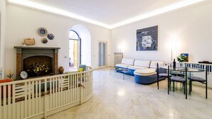 Una sala de estar con chimenea, un sofá, una mesa de comedor con sillas y una barandilla blanca.