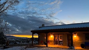 Ein gemütliches Haus mit überdachter Veranda, warmem Licht im Inneren und verschneiter Landschaft im Hintergrund.
