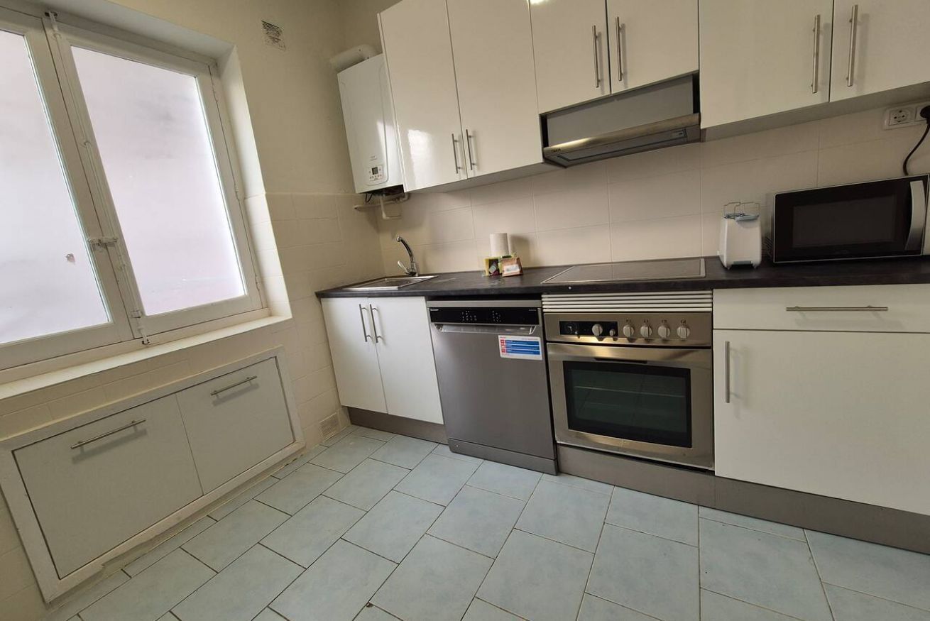 A kitchen with white cabinets, a dishwasher, an oven, a microwave, and a window.