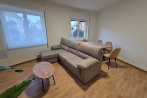 Una habitación con un sofá modular, una mesa redonda y una mesa de comedor con sillas.
