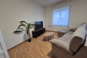 Ein Wohnzimmer mit einer Couch, einem Fernseher, einem Couchtisch und einer Topfpflanze.