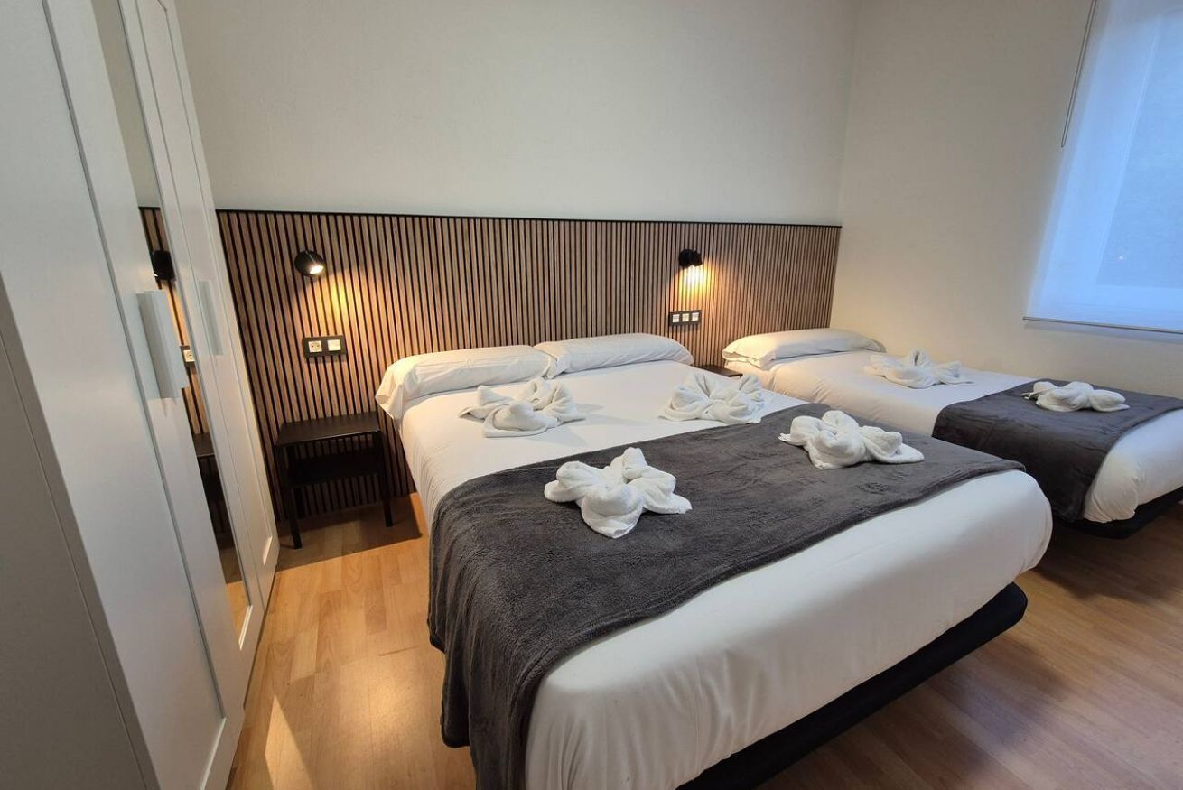 Ein Hotelzimmer mit zwei Betten, einem hölzernen Kopfteil, Wandleuchten und einem Fenster.