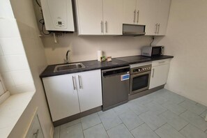 Eine Küche mit weißen Schränken, einem Geschirrspüler, einem Backofen und einer Mikrowelle.