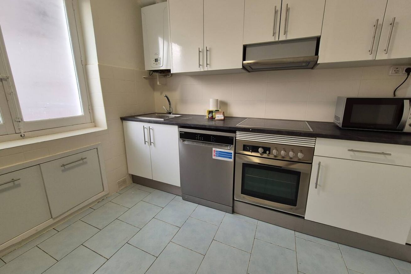 A kitchen with white cabinets, a dishwasher, an oven, a microwave, and a window.