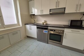 A kitchen with white cabinets, a dishwasher, an oven, a microwave, and a window.