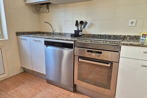 Een keuken met een vaatwasser, oven, granieten aanrechtblad en witte kasten.