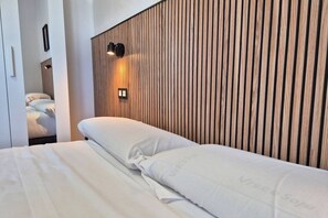 Een hotelkamer met een wand van houten latten, een bed met wit beddengoed en een wandlamp.