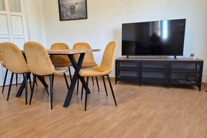 Un coin repas comprenant une table et quatre chaises, un téléviseur à écran plat et un meuble de rangement noir pour les appareils multimédias.