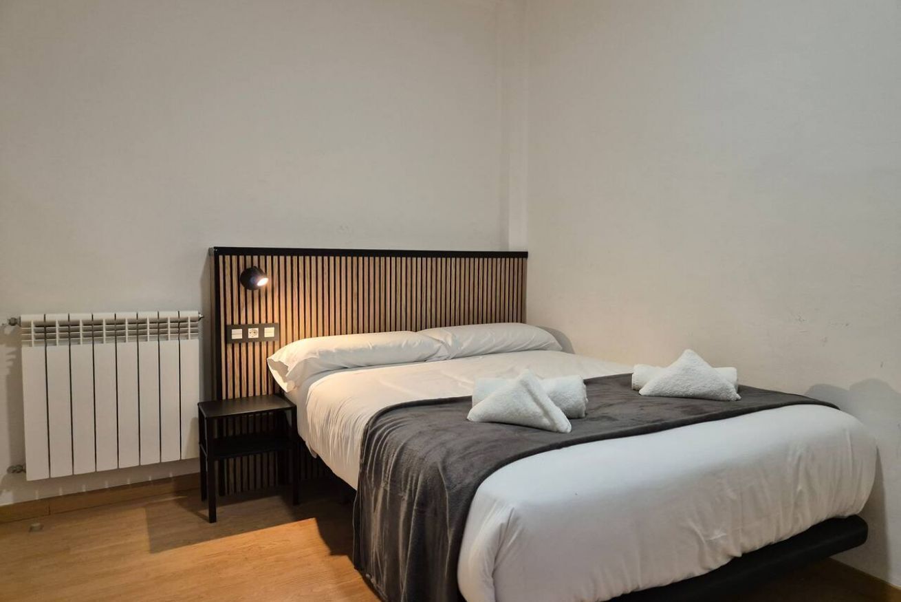 A bedroom with a bed, bedside table, and a wall-mounted light.