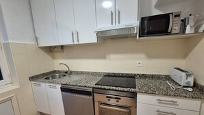 Eine kompakte Küche mit weißen Schränken, einem Geschirrspüler, einem Backofen, einer Mikrowelle und einem Toaster.