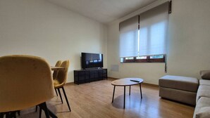 Ein modernes Wohnzimmer mit einer Couch, einem runden Couchtisch, einem Fernseher und einem Fenster mit Jalousien.