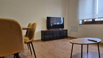A room with a television on a stand, a round table, and two chairs.