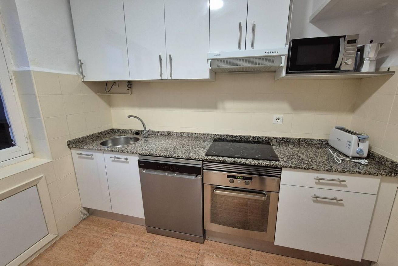 Een compacte keuken met witte kastjes, een vaatwasser, een oven, een magnetron en een broodrooster.