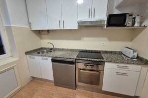 Una cocina compacta con armarios blancos, lavavajillas, horno, microondas y tostadora.