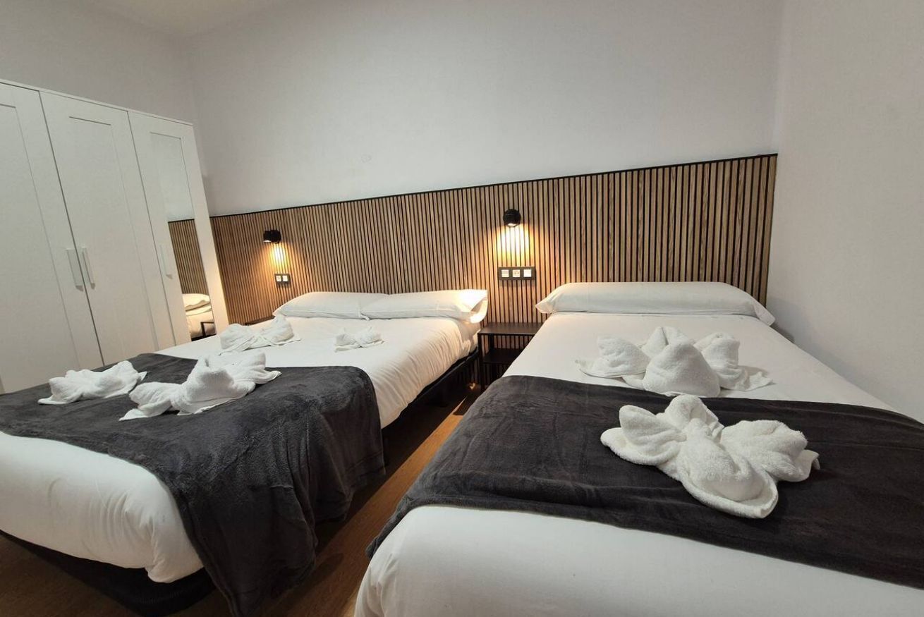 Une chambre d’hôtel avec deux lits, une armoire et des lampes fixées au mur.
