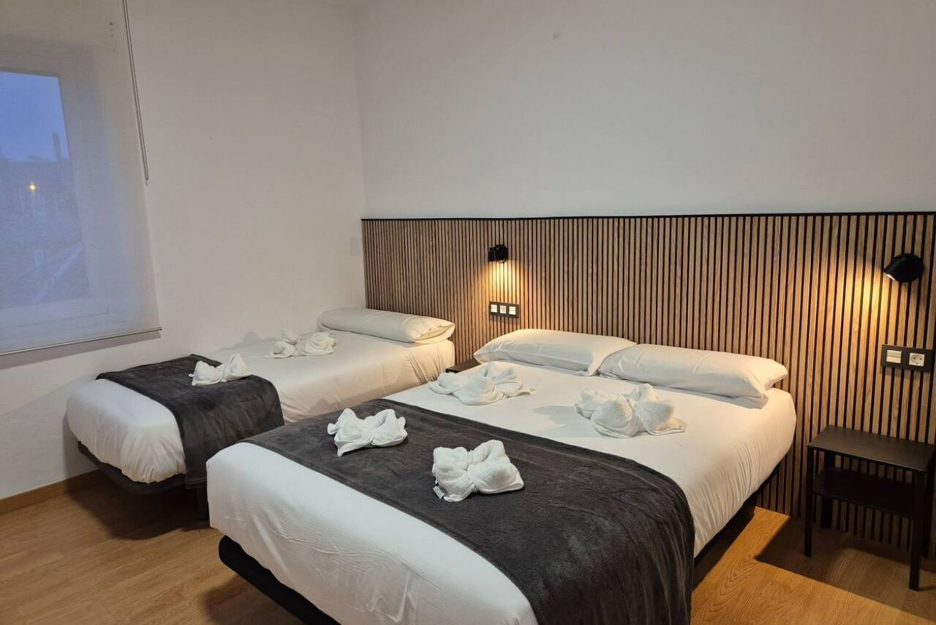 Een hotelkamer met twee bedden, een houten hoofdbord, een klein tafeltje en een projectiescherm.