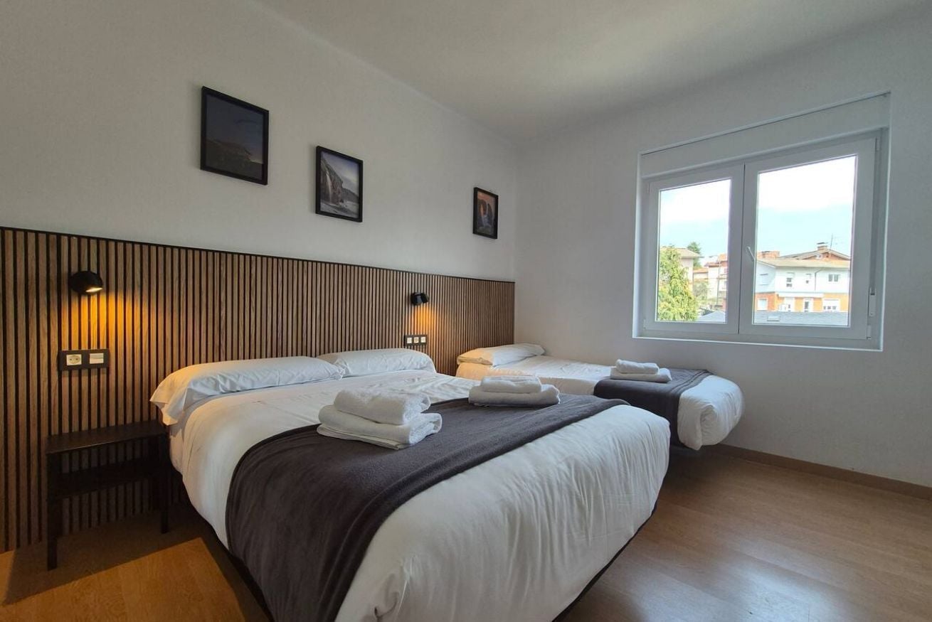 Ein Hotelzimmer mit zwei Betten, einem Holzkopfteil, Wandleuchten, einer Sitzbank und einem Fenster mit Blick.