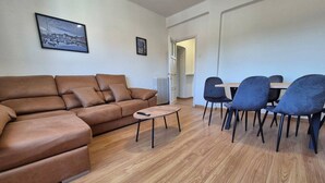 A living room with a brown sofa, a small round table, and a dining area with chairs.