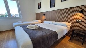 A hotel room with two beds, a wooden headboard, a small table, and a window with a view.