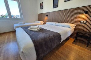 A hotel room with two beds, a wooden headboard, a small table, and a window with a view. - 648C2 Apartamento Mareval (Oviedo)