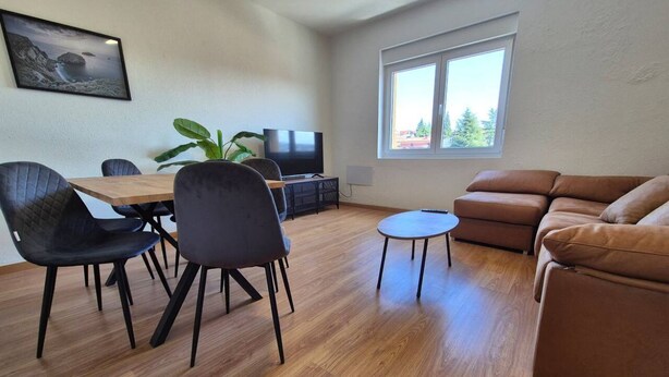 A living room with a sofa, a dining table with chairs, a TV, and a window with a view.