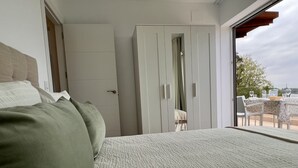 A bedroom with a large bed, a wardrobe, and a balcony with a table and chairs.