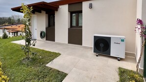 A modern house with a white exterior, a brown roof, and a Vaillant air conditioning unit on the porch.