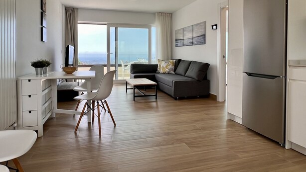 Eine moderne Wohnung mit Essbereich, einer Couch, einer Küche und einem großen Schiebeglastür, die auf einen Balkon mit Stadtblick führt.