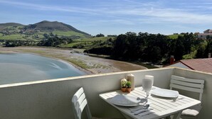 Een balkon met een tafel voor twee, met uitzicht op een rivier en groene heuvels.