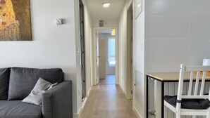 A modern living room with a grey sofa, a dining table with a chair, and a hallway leading to a bathroom. - Cozy apartmet in Hoznayo (Entrambasaguas)