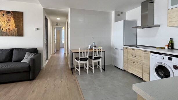 A modern kitchen with a built-in washing machine, a dining area with a table and chairs, and a living room with a sofa and a painting on the wall. - Cozy apartmet in Hoznayo (Entrambasaguas)