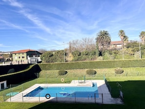 A swimming pool with a fence, a grassy area, and a building with a red roof in the background.