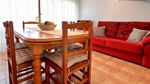 Un comedor con mesa y sillas de madera, un sofá rojo y una ventana con cortinas.