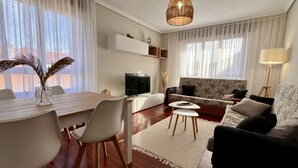 Una sala de estar moderna con comedor, un juego de sofás, televisor y una lámpara colgante.