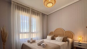 Un dormitorio con una cama grande, una mesita de noche con lámpara y una ventana con cortinas de encaje.