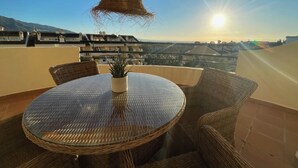 A round table with wicker chairs and a potted plant on a balcony overlooking a cityscape during sunset. - 2-Bed Sea View Apt, 10 mins from Puerto Banus (Nueva Andalucia)