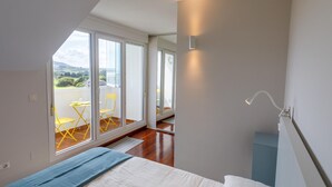 Une chambre à coucher avec un lit, une couverture bleue et une vue sur un balcon avec des chaises jaunes.
