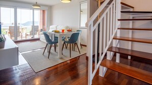 Un espace de repas moderne avec un escalier en bois, une table à manger avec des chaises et une vue dégagée grâce à de grandes fenêtres.