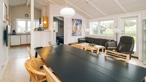 A modern kitchen with white cabinets, a dining area with a black table, and a living room with a sofa and chairs. - 4 Star Holiday Home in Korsor (Korsor)