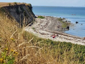 A beach with a cliff, rocky shore, and calm sea.