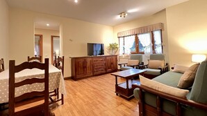 Un ampio soggiorno con pavimento in legno, zona pranzo con tavolo e sedie, divano, televisore e finestra con tende.