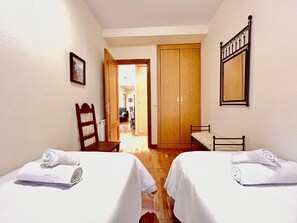 Habitación de hotel con dos camas, un armario de madera, una mesita pequeña y una silla.