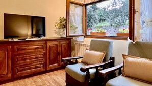 Un soggiorno con un mobile in legno, una televisione, due poltrone e una finestra vista verde.
