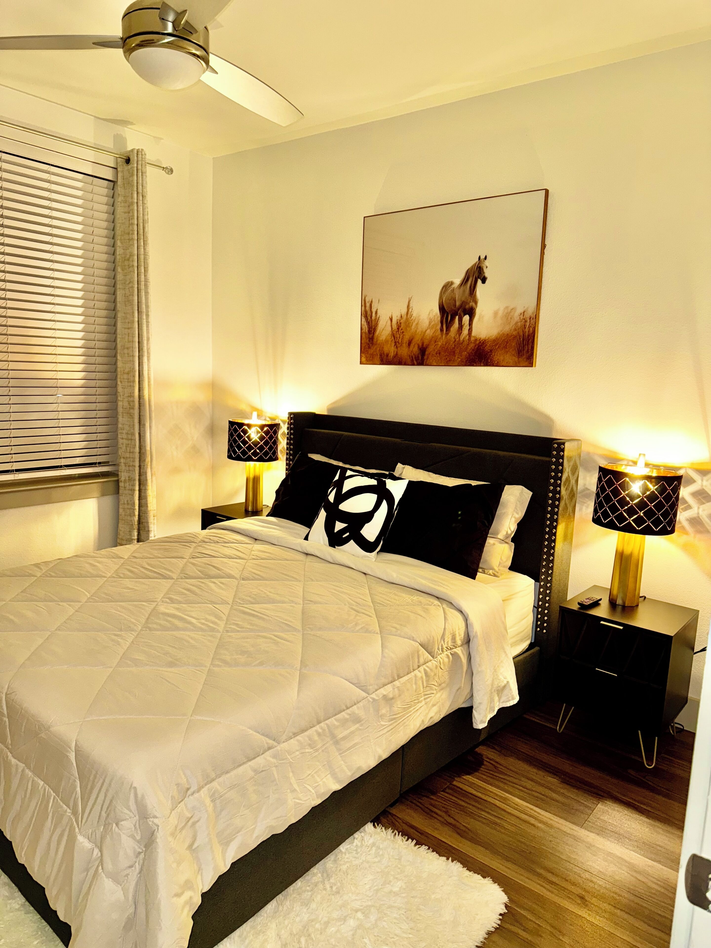 A neatly arranged bedroom with a bed, a headboard, bedside tables, a lamp, a painting, and a ceiling fan.